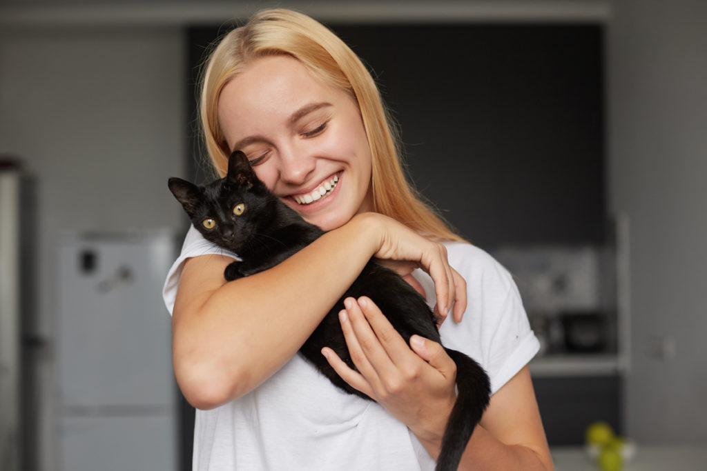 happy young blonde woman kitchen holds hands caresses stroking hugs black little cat cute tenderly smiling 1024x683 - Budeme mať mačku: Aké vybavenie budeme potrebovať?